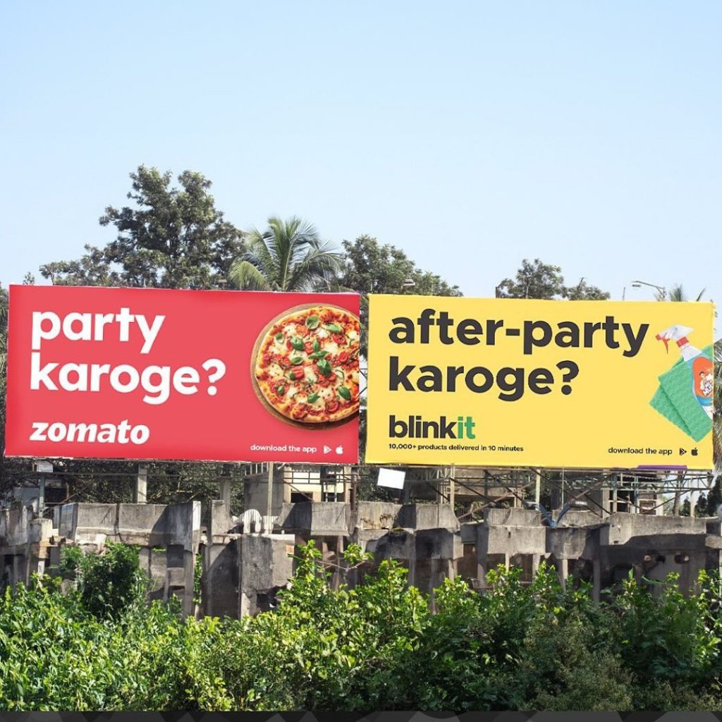 Zomato and Blinkit billboards placed side by side showing a creative guerrilla marketing campaign in India with connected messaging about party food and after-party needs